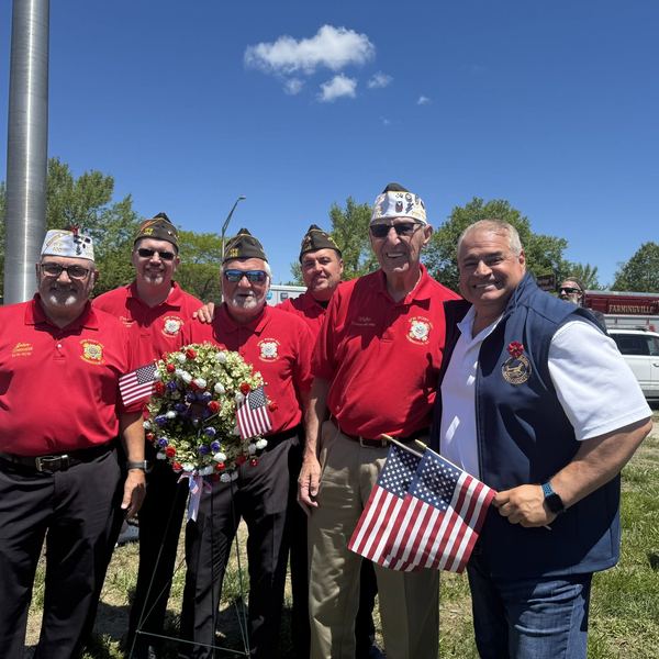 Post 400 members in red shirts holding a wreath and small flags at the Memorial Day parade