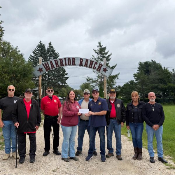 Post 400 members standing under the Warrior Ranch entrance sign